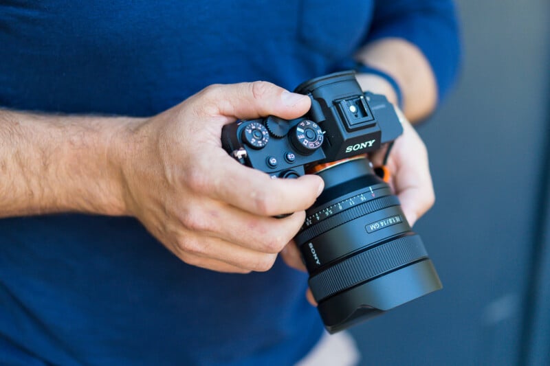 A close-up of a person's hands adjusting the settings on a sony DSLR camera, focusing on the dials and lens. the background is blurred, highlighting the details of the camera.