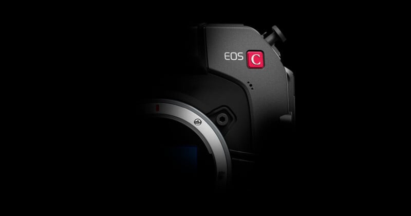 A partially lit camera against a black background, showing the "EOS C" label and part of the lens mount area. The rest of the camera body fades into the darkness.