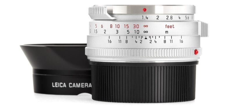 A leica camera lens with a focus ring marked in feet and meters, alongside a detachable lens hood, isolated on a white background.