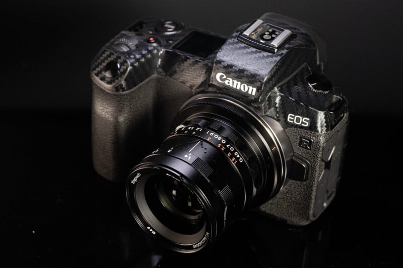 A Canon EOS R camera with a black lens mounted, set against a reflective black background, highlighting its sleek design and advanced features.