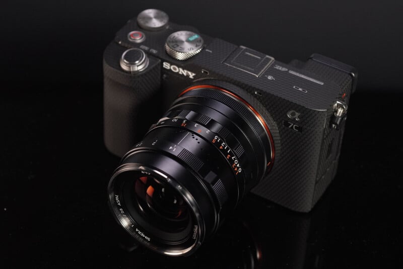 A Sony mirrorless camera with a textured grip and a vintage-style lens positioned on a reflective black surface.