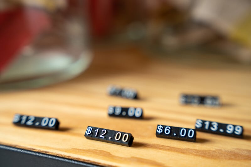 Price tags with different values such as $12.00 and $6.00 in selective focus on a wooden table, with a blurred background suggesting a shopping or market setting.
