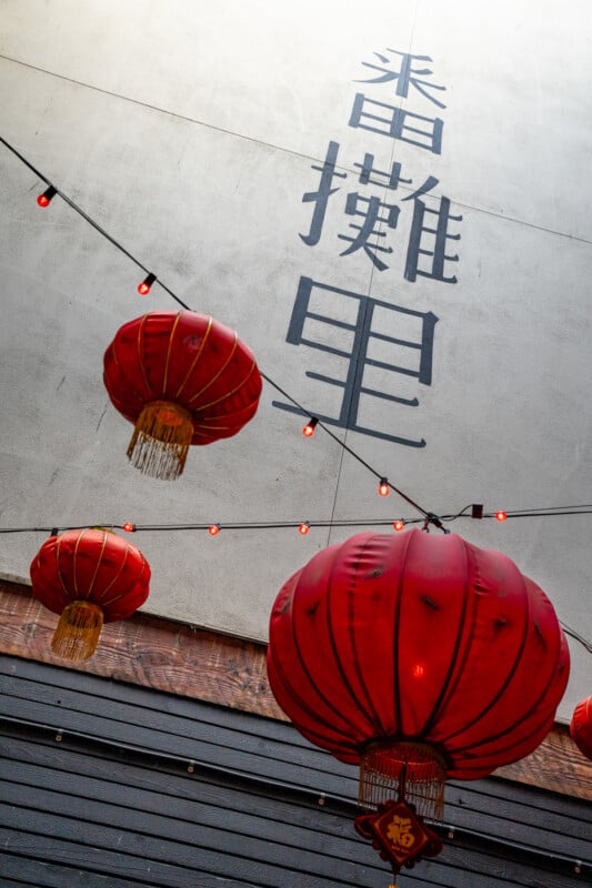 Red lanterns hanging from a string against a building wall with large Chinese characters painted in black, creating a traditional and festive atmosphere.