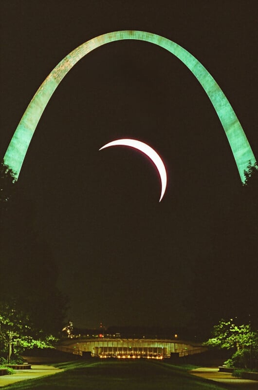 A solar eclipse visible through the gateway arch in st. louis, showing a crescent sun aligned symmetrically under the illuminated arch at night.