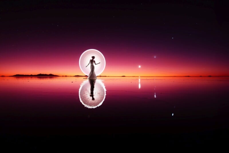 A person stands on a vast reflective surface at sunset, creating the illusion of walking on water. The sky is vibrant with deep shades of purple, pink, and orange. Bright, circular light trails surround them, and distant stars are visible in the twilight sky.