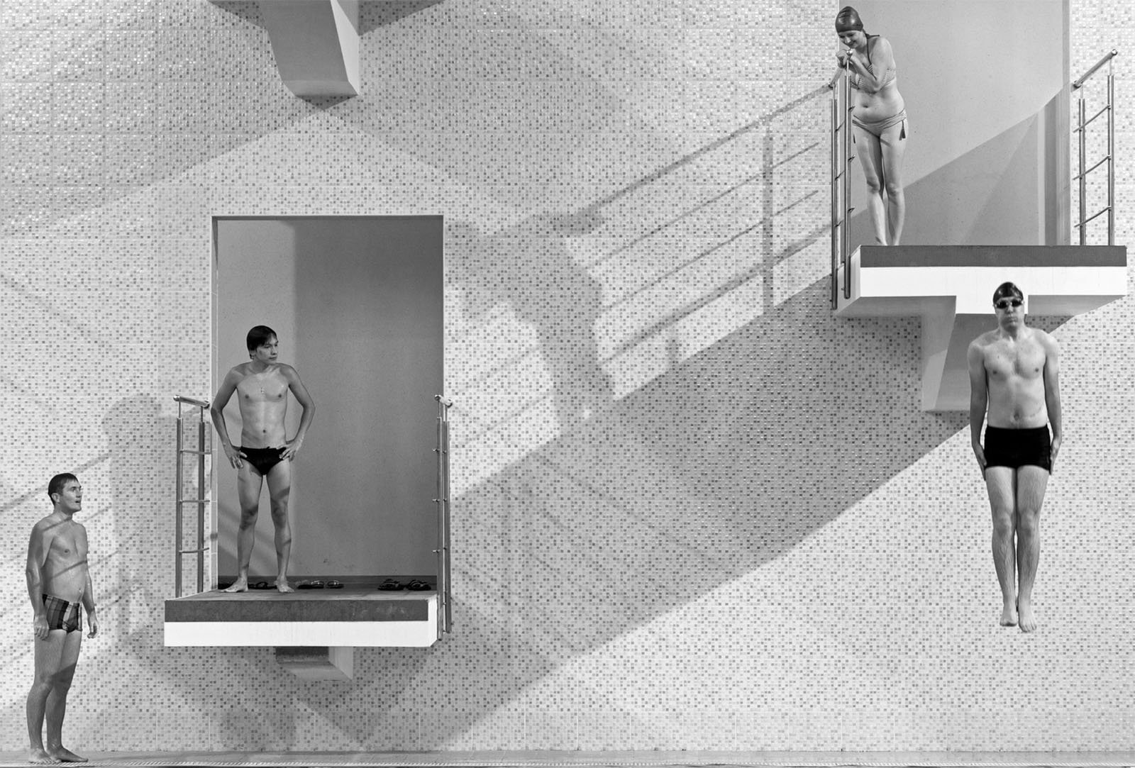 A black and white image shows four divers on a diving platform. One diver stands on the left, observing. Another stands on a lower platform slightly to the right. One more covers his face on the upper right platform, while a last diver jumps off from a height.