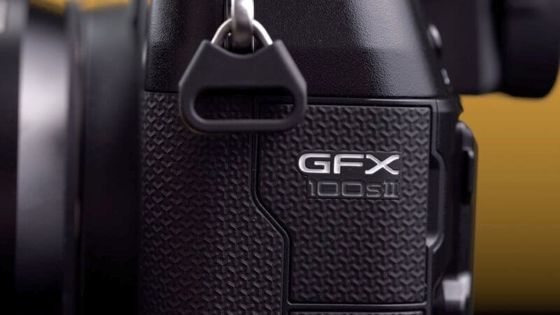 Close-up view of a black GFX 100S camera with textured surface, focusing on the model label, against a blurred yellow background.