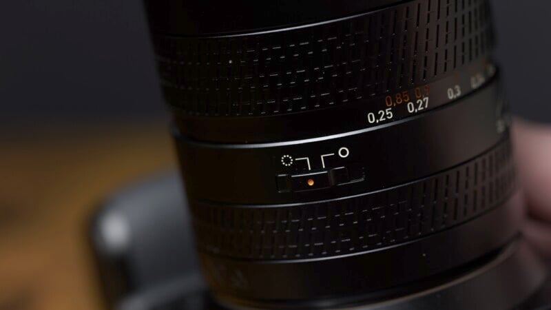 Close-up of a camera lens showing detailed focus distance and aperture scales, with a blurred dark background.