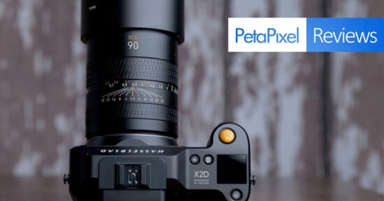A hasselblad x2d camera with a large lens attached, positioned on a wooden surface with a blurred background, showcasing the "petapixel reviews" logo overlaid on the image.