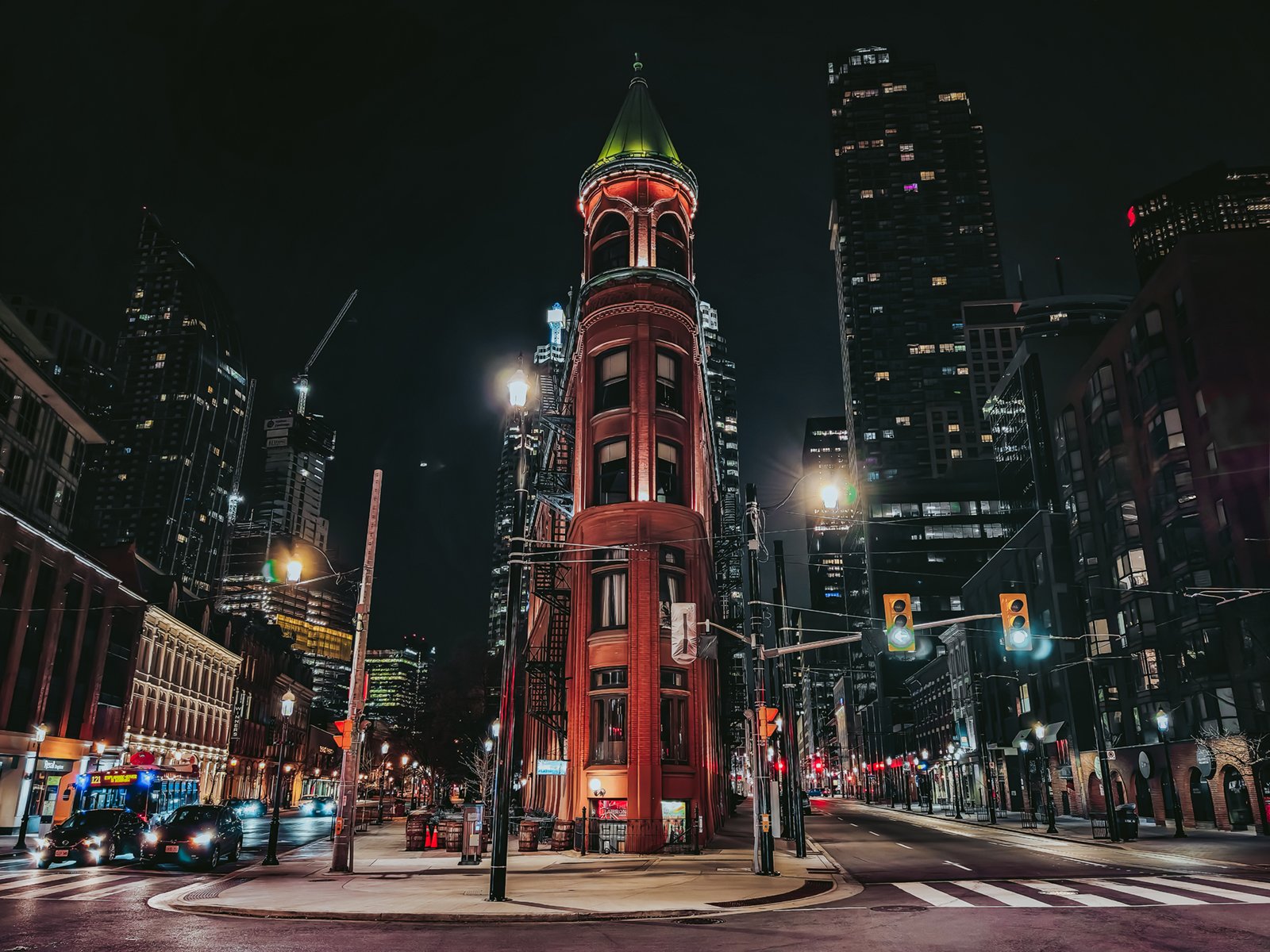 A nighttime view of the historic gooderham building in toronto, showing its distinctive flatiron shape and red brick facade, illuminated by street lights with modern skyscrapers in the background.