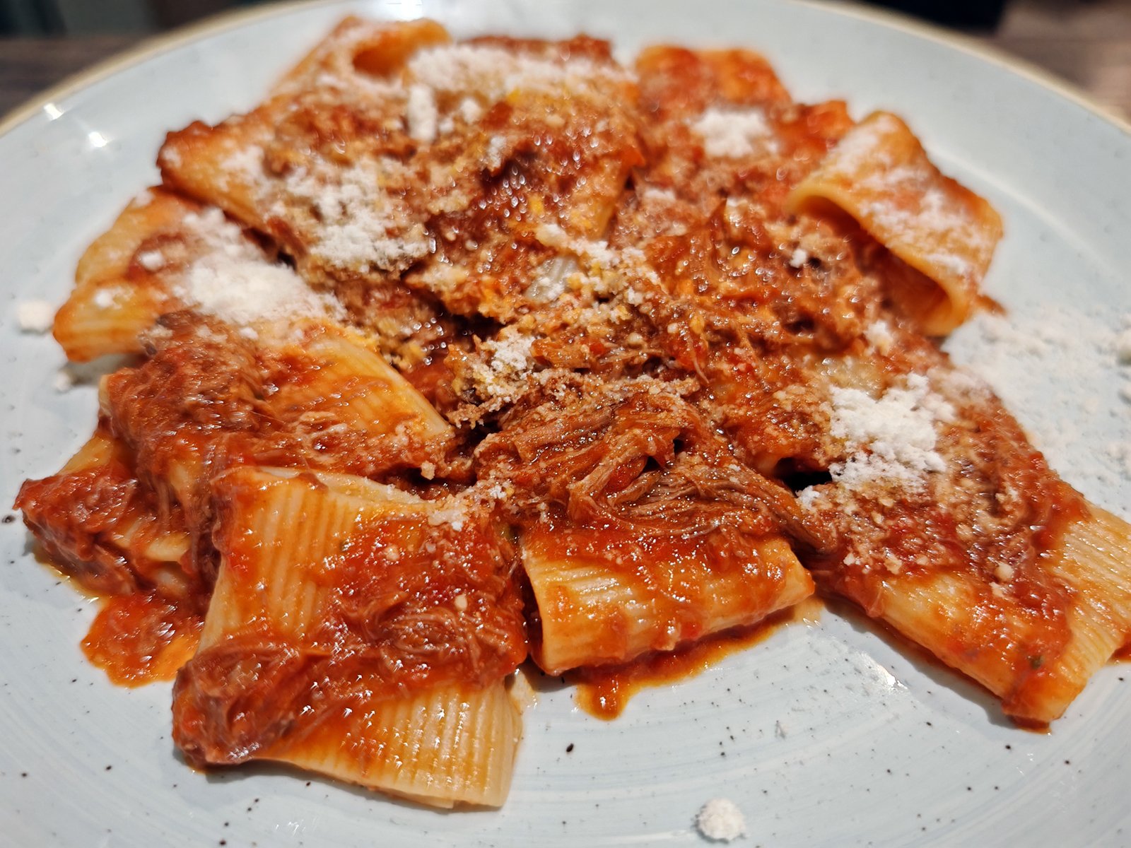 A plate of rigatoni pasta with a rich tomato sauce and shredded meat, topped with a generous sprinkling of grated parmesan cheese.