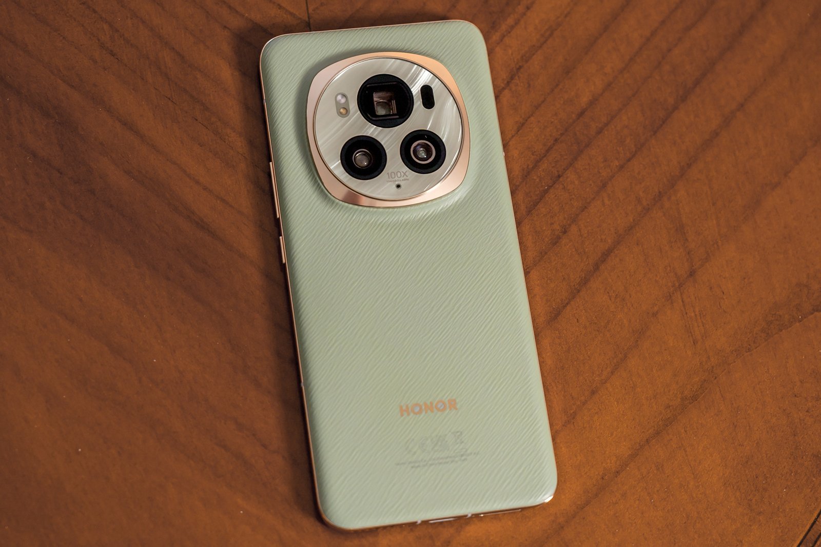 A mint green honor smartphone lying on a wooden surface, featuring a prominent circular camera module with multiple lenses.