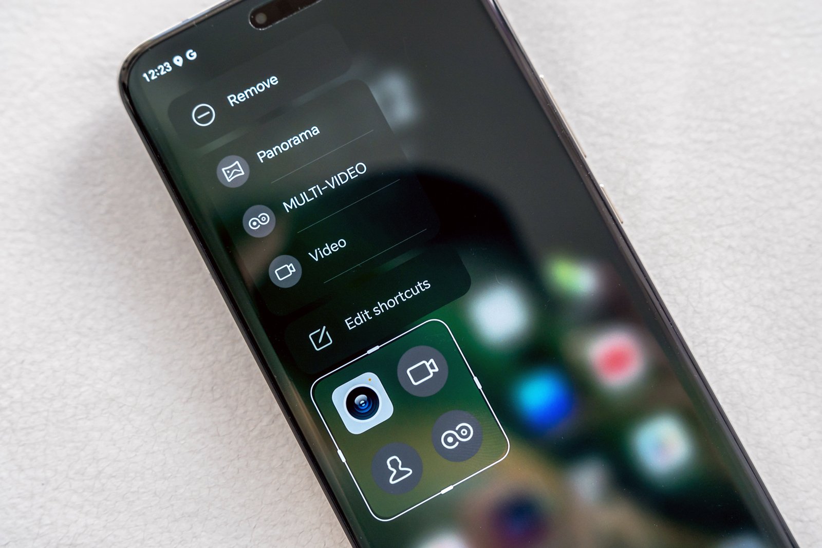 Close-up of a smartphone screen displaying camera settings with options for video, panorama, and multi-video on a blurred app icon background.