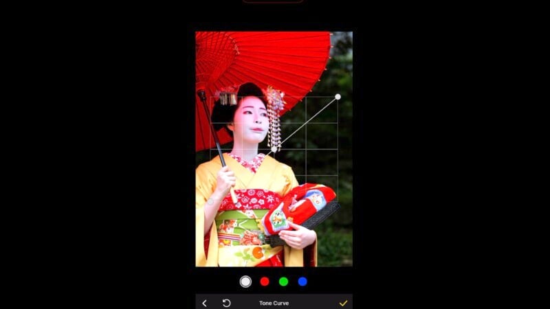 A person is dressed in traditional Japanese attire, holding a vibrant red umbrella and wearing ornate hair accessories. The photo shows a color editing interface with tone curves and color options, suggesting the image is being edited.