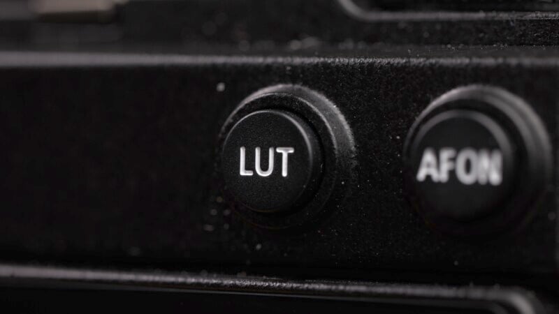 Close-up of a black button labelled "LUT" on an electronic device. The button is prominently featured in the center of the image, with another partially visible button labeled "AFON" on the right side. The surrounding surface appears to be textured.
