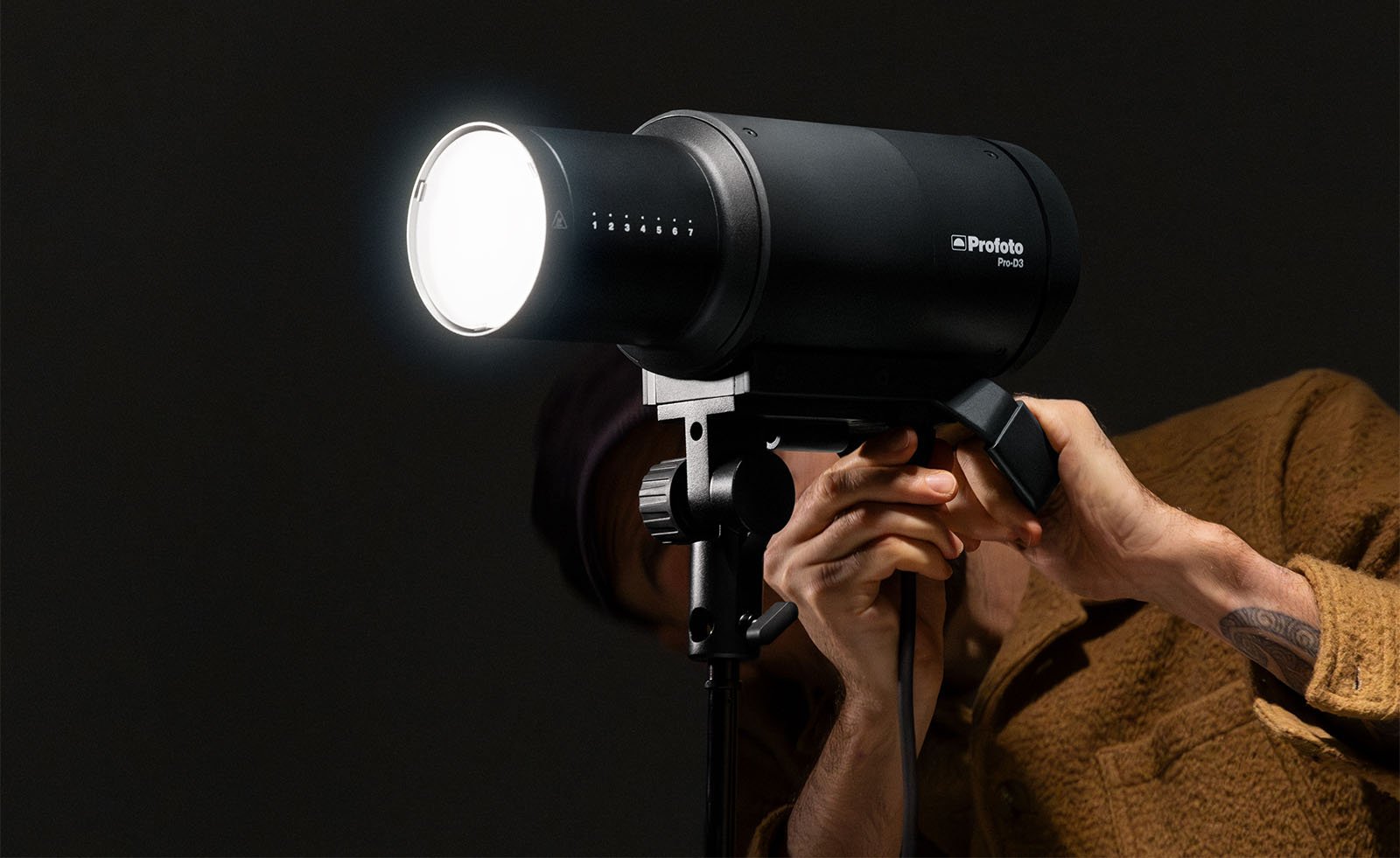 A person adjusts a large profoto pro-11 studio flash mounted on a stand against a dark background, focusing the device with their hands.