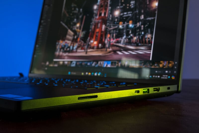 A close-up view of an open laptop showing an image editing application on its screen. The image displayed on the screen depicts a night cityscape with bright lights and buildings. The laptop has several ports visible on the side, including USB and HDMI ports.