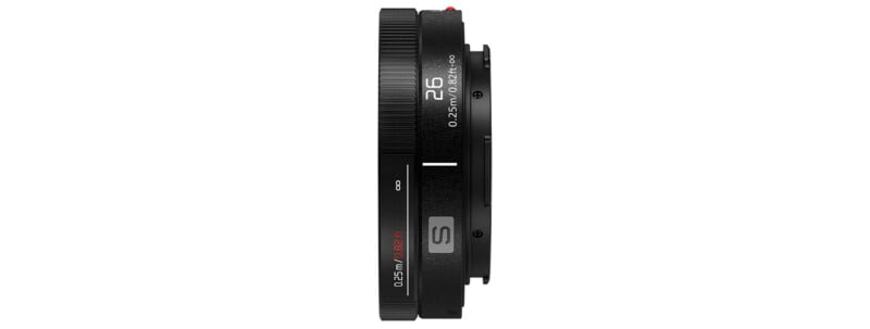 Side view of a black camera lens with markings showing "26 mm" and "0.25m/0.82ft." The lens has textured focus and zoom rings, with a small red indicator and the letter "S" on the side. The design is sleek and compact.