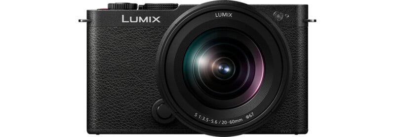 A black Lumix digital camera is shown from the front, featuring a prominently large lens with specifications 3.5-5.6/20-60mm. The camera's body has a textured grip, and the lens has a glossy finish, reflecting light. The brand name LUMIX is displayed on the upper left.