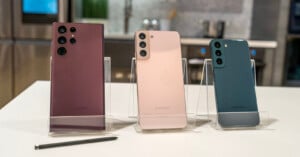 Four samsung smartphones, each a different color, displayed on stands in a modern kitchen setting, with models ranging from light pink to dark green.
