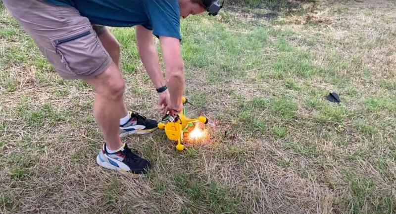 A man outdoors lights a small, bright flame on a yellow object placed on dry grass, using a lighter in his hand. he is wearing shorts and sneakers.