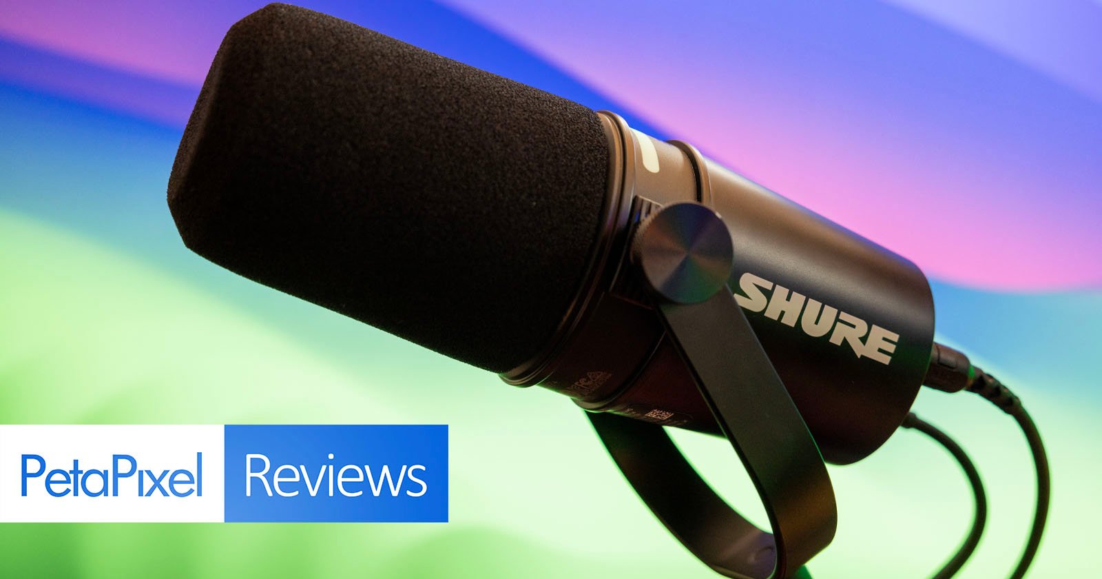 A close-up image of a black shure microphone with its brand logo visible, positioned against a colorful blurred background, with the text "petapixel reviews" overlaying the bottom corner.