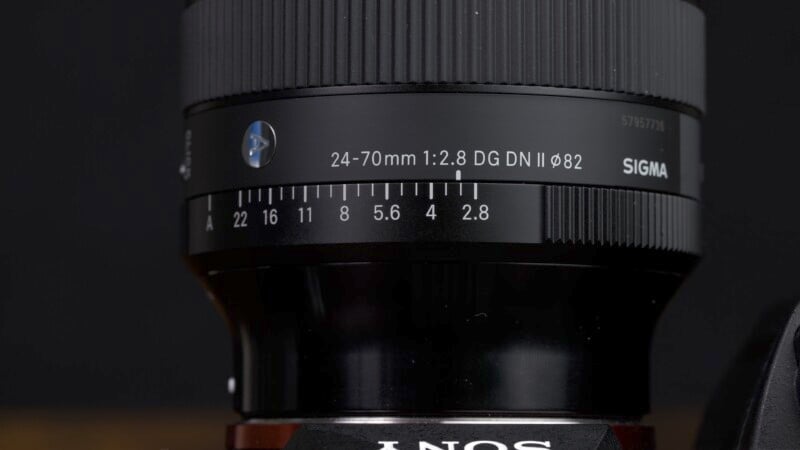 Close-up of a Sigma 24-70mm f/2.8 lens mounted on a camera, focusing on the aperture and focal length details on the lens barrel.
