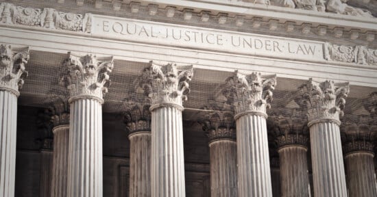 Front exterior of a neoclassical building featuring a row of Corinthian columns and the engraving "Equal Justice Under Law" on the frieze.