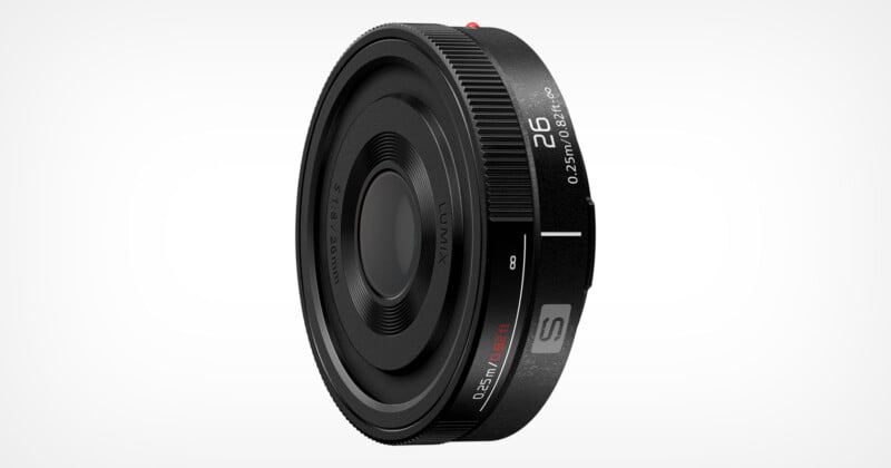 A close-up view of a Lumix S 26mm camera lens. The lens has a sleek, black design with various engraved markings indicating focal length and aperture settings. It is set against a plain, white background.