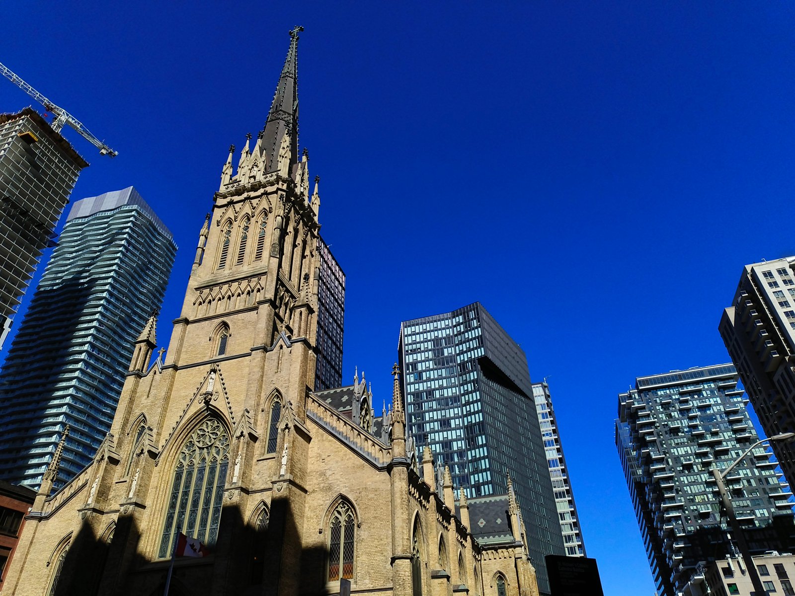 A gothic-style church with a tall spire stands prominently among modern skyscrapers under a clear blue sky.