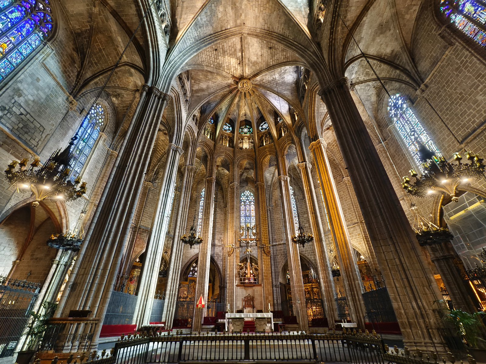Interior of a gothic cathedral with soaring vaulted ceilings, stained glass windows, and a detailed altar bathed in soft light. the structural columns and ornate lamps add to the historical ambiance.