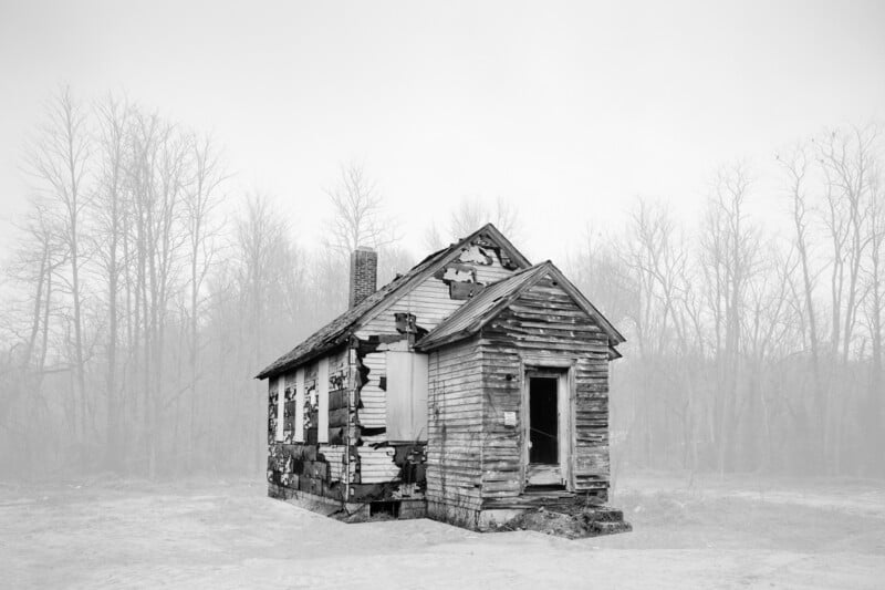 An old, dilapidated wooden house with peeling paint and boarded-up windows, set in a barren landscape under a foggy sky.