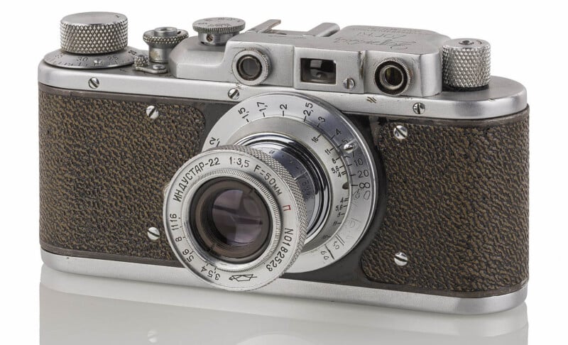 A vintage Zorki rangefinder camera with a brown textured grip and a silver lens. Markings around the lens indicate aperture and focus settings. The camera has various dials and knobs on the top, and it is set against a plain white background.