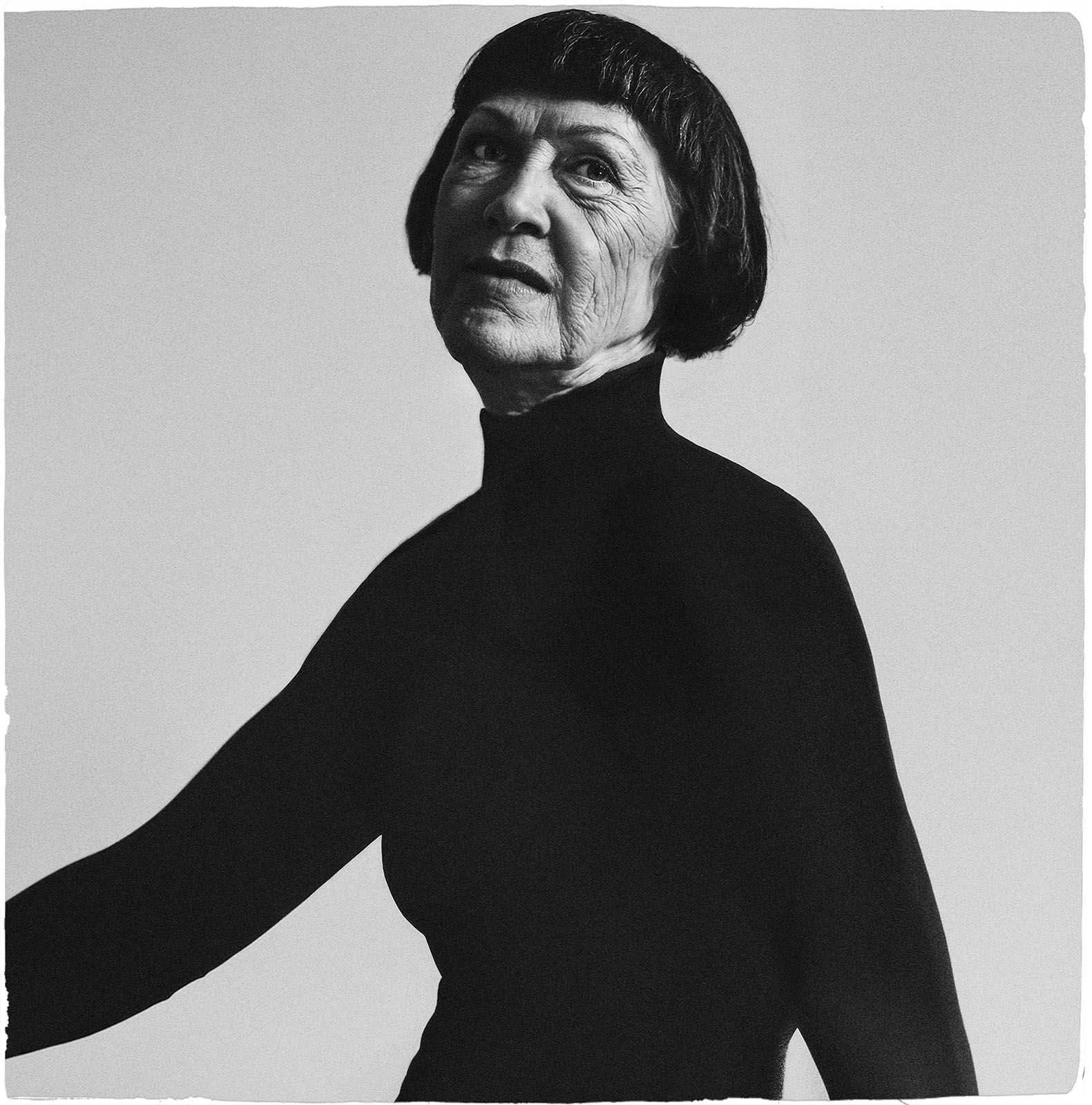 A monochrome portrait of an elderly woman with short dark hair, wearing a black turtleneck. she is looking to her right with a thoughtful expression.