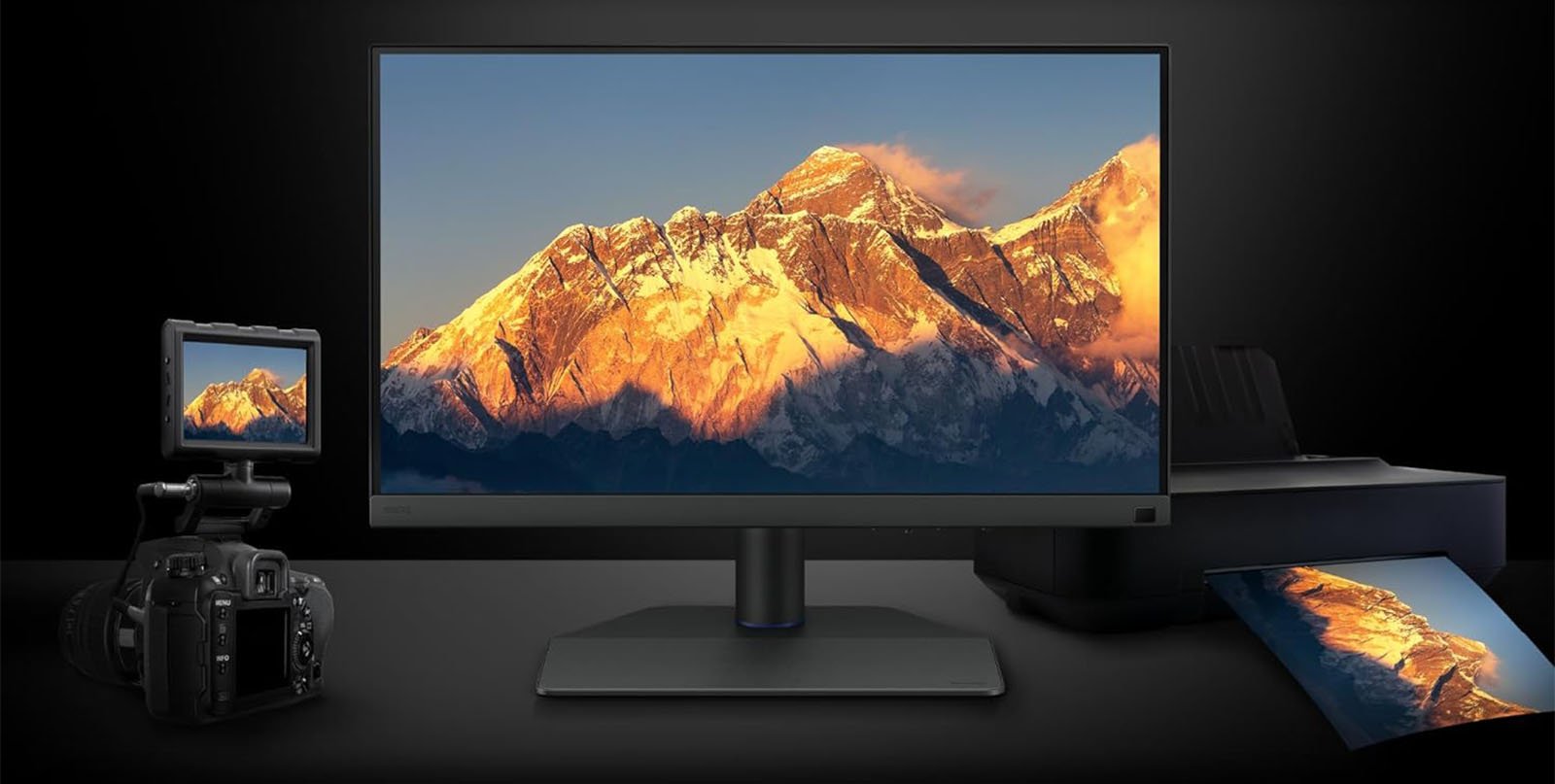 A desktop setup featuring a monitor displaying a mountain landscape, flanked by a dslr camera on the left and printed photographs on the right, all against a dark background.