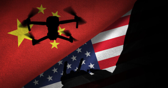 A silhouette of a drone and a remote control against a backdrop of the Chinese and American flags, symbolizing the technological and political rivalry between China and the United States. The Chinese flag is on top and the American flag is at the bottom.