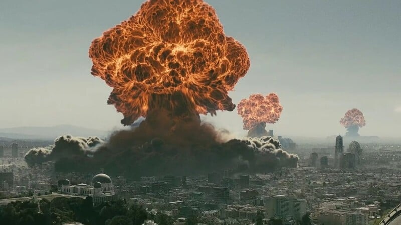 A cityscape is engulfed by multiple, massive explosions, creating large mushroom clouds of fire and smoke rising into the sky. Skyscrapers can be seen in the foreground with a dense urban area spreading out below the fiery plumes.