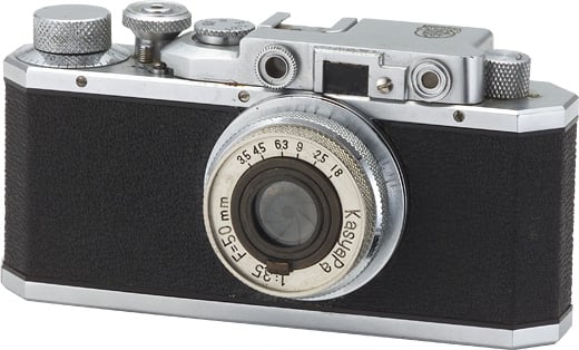A vintage rangefinder camera with a black and silver body. The camera features a prominent lens marked with various focal lengths and the brand name "Kasyap." The top has several dials and a viewfinder.