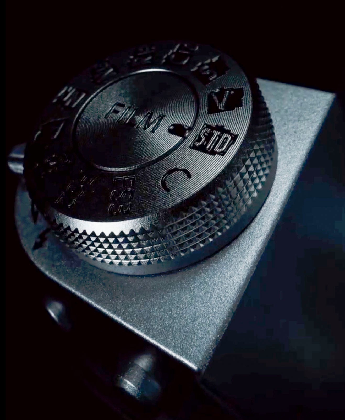 Close-up of a camera's mode dial showing various settings such as auto, p, tv, av, and m, highlighted by moody lighting against a dark background.