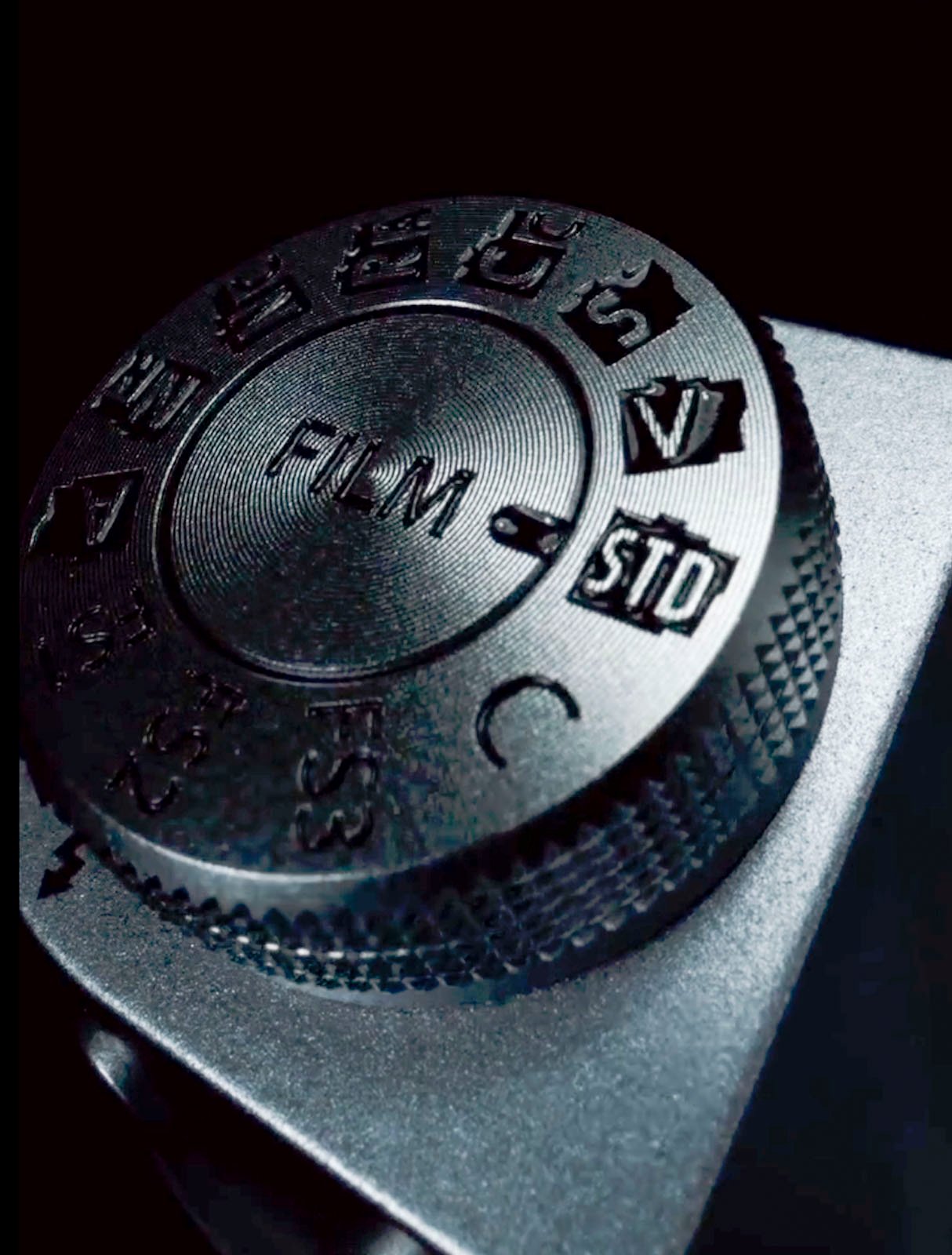 Close-up of a camera mode dial showing various settings such as auto, manual, and video, set against a black background.