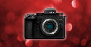 A Panasonic Lumix G9 camera is centered against a red, bokeh background. The camera body is black with a textured grip, various control buttons, and the "LUMIX G9" label prominently displayed above the lens mount.