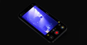 A smartphone with a video editing app displayed on the screen. The app interface includes various video controls and a timeline. The video being edited shows a scene with a DJ performing on stage under blue lighting. The background is black.