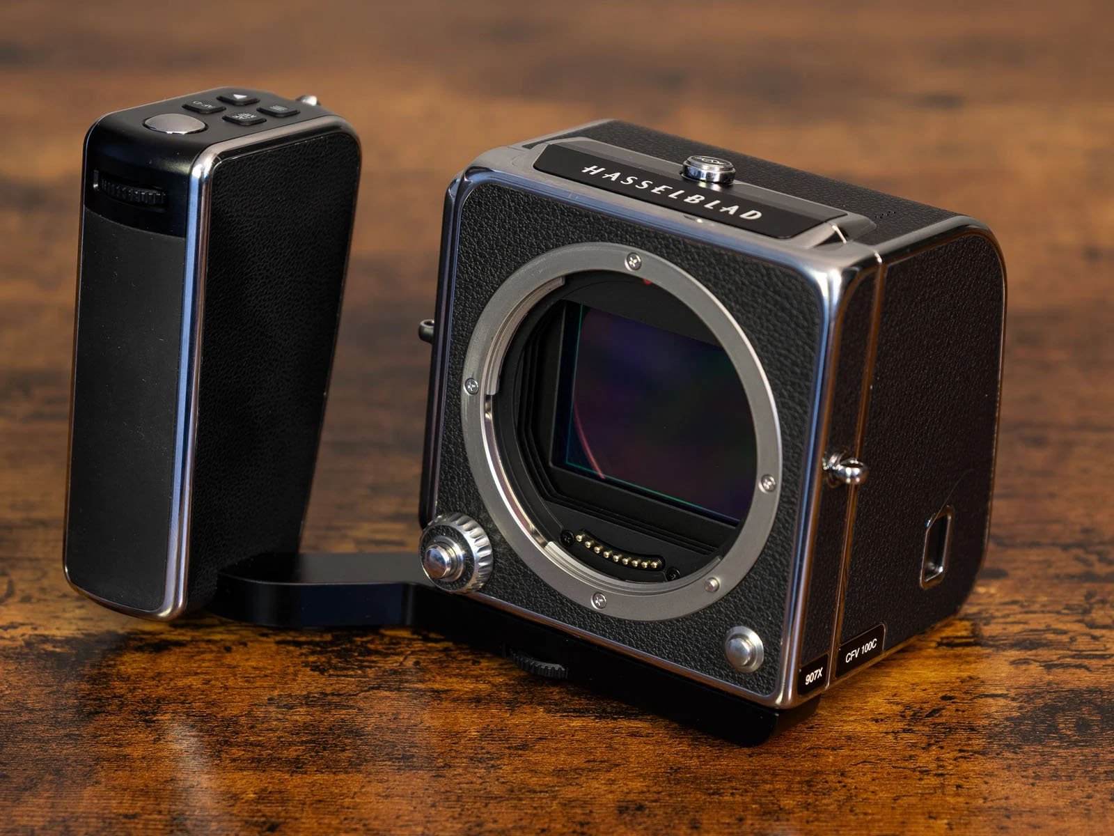 A hasselblad medium format camera body with a digital back on a wooden surface, showing a detailed view of the camera's lens mount and sensor.
