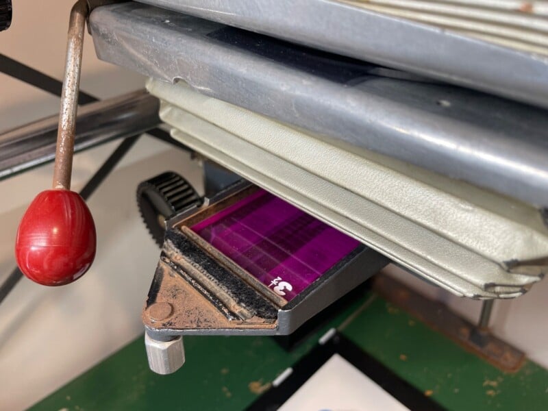 Close-up of a purple etched circuit board undergoing a manufacturing process on a mechanical press, focusing on the etching details and machinery elements.