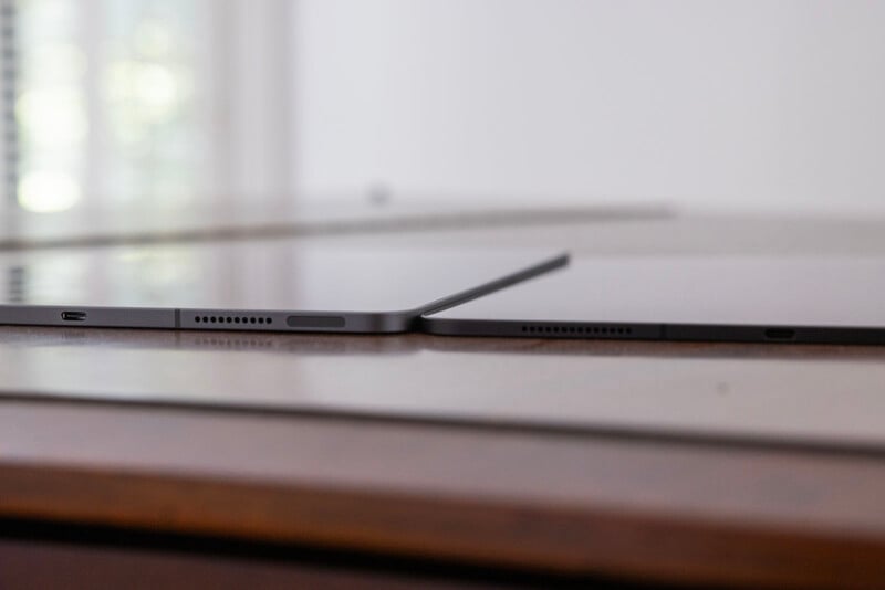 Close-up of two iPad Pros side by side on a wooden surface, focusing on their side profiles showing USB-C ports and a sleek design.