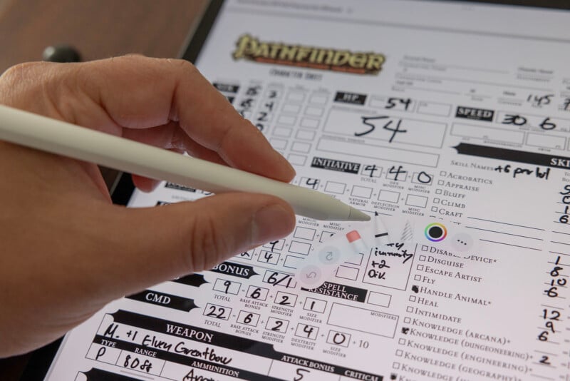 A hand holding a pencil marks a character sheet from the tabletop role-playing game Pathfinder, with various stats and information visible.