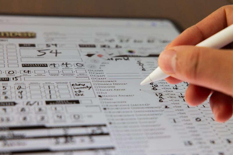 Close-up of a hand holding a pen over a detailed Dungeons & Dragons character sheet, filing in attributes and stats.
