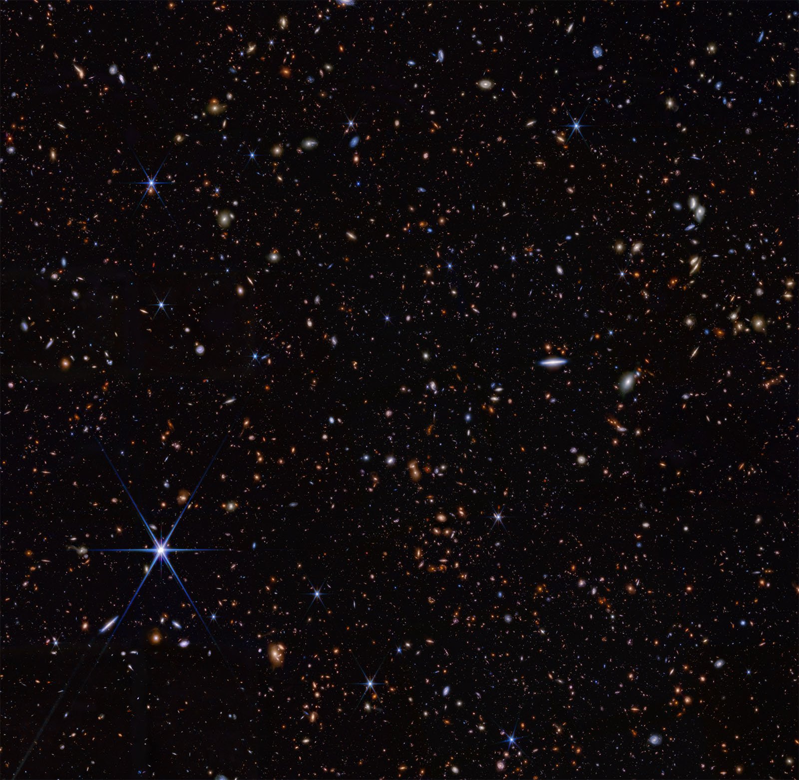 An image of a dense star field in deep space, filled with countless stars and distant galaxies. The stars vary in brightness and color, with some exhibiting a starburst effect. The background is mostly dark, highlighting the luminous points scattered throughout.