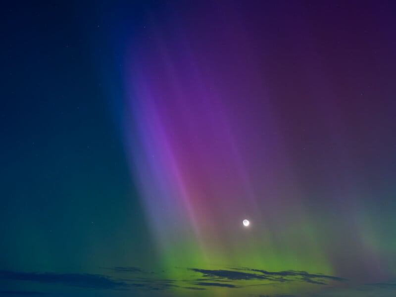 A vibrant display of the northern lights in a clear night sky, with vivid colors ranging from deep violet to bright green, alongside a visible moon.