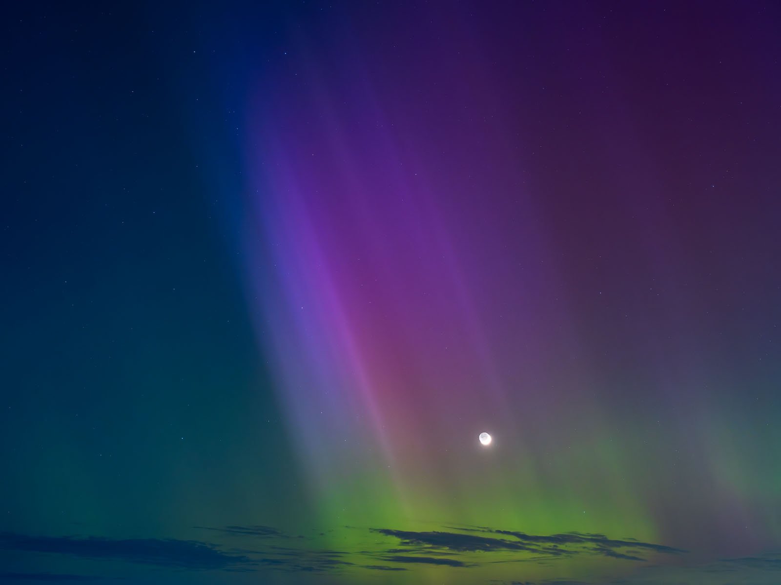 A vibrant display of the northern lights in a clear night sky, with vivid colors ranging from deep violet to bright green, alongside a visible moon.
